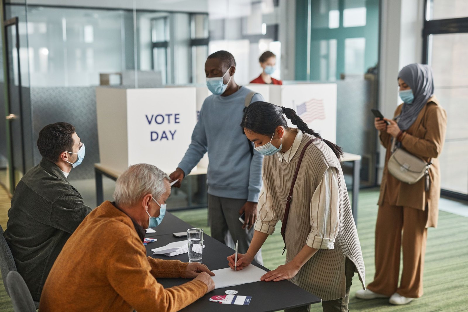 service-1-1 A diverse group of adults casting votes indoors on election day, maintaining safety protocols.
