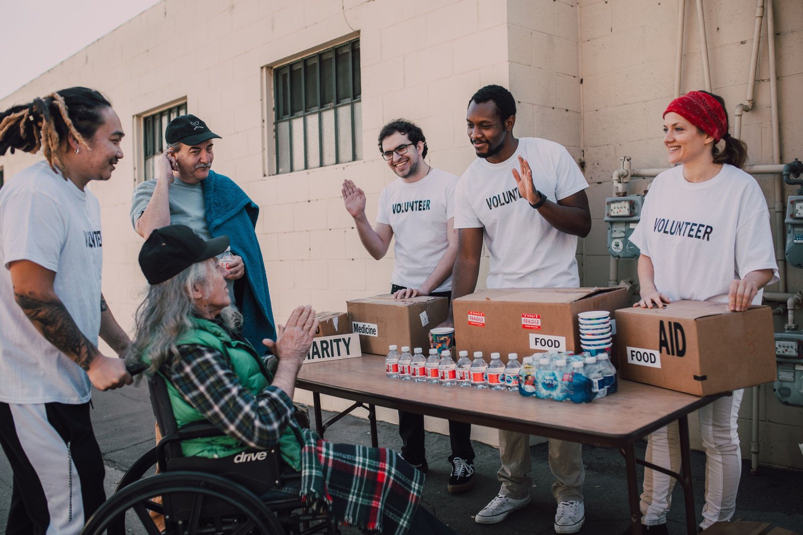 service-1-1 Group of volunteers providing food and aid to a person in wheelchair outdoors.