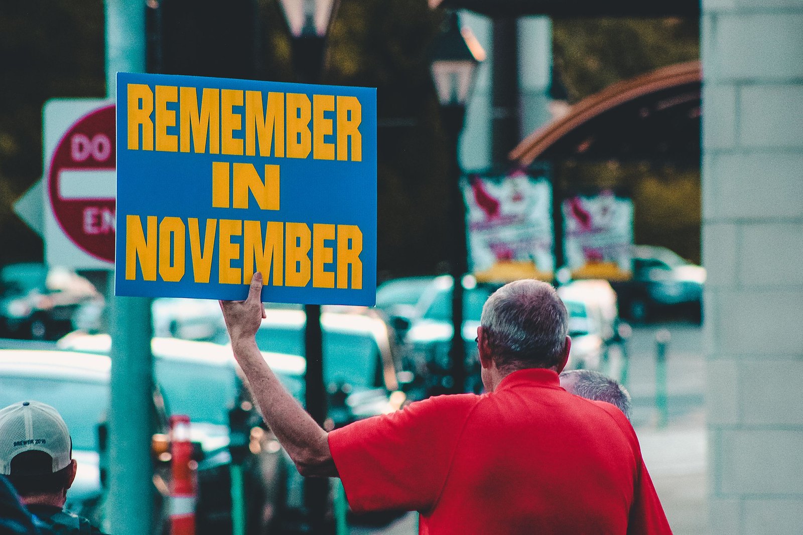 service-1-1 Man holding 'Remember in November' sign on urban street during the day.