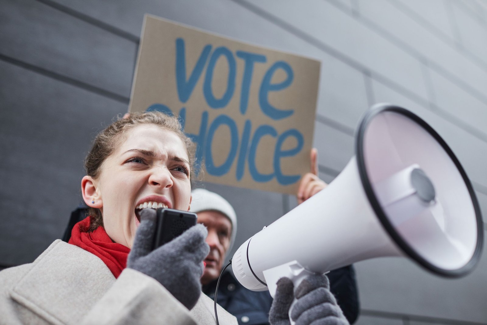 service-1-1 Woman passionately speaking through a megaphone during a winter protest with a visible vote choice sign.